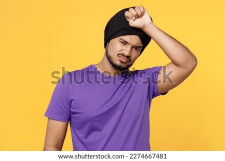 Sick ill tired exhausted devotee Sikh Indian man ties traditional turban dastar wear purple t-shirt put hand on forehead isolated on plain yellow background studio portrait People lifestyle concept
