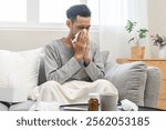 Sick, influenza asian young man have fever, hand blowing nose, sneezing in tissue at home while ill male suffering from flu sitting under blanket on couch. Health care with disease, pandemic virus.