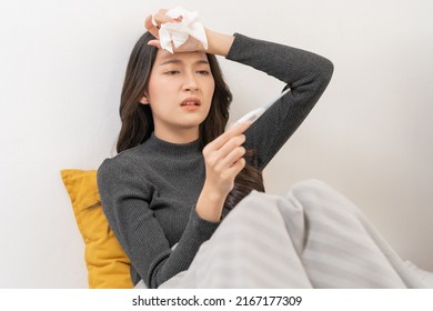 Sick, influenza asian young woman, girl headache have a fever, flu and check thermometer measure body temperature, feel illness sitting on sofa bed at home. Health care person on virus, covid-19.