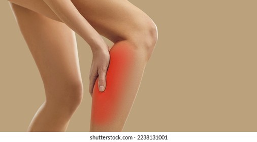 Sick or injured woman experiencing calf muscle pain standing isolated on beige background. Close up of woman's leg with injury caused by sports accident or arthritis, sore spot is marked in red