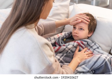 Sick little boy covered in blanket is lying on couch while his mother is taking his temperature - Powered by Shutterstock