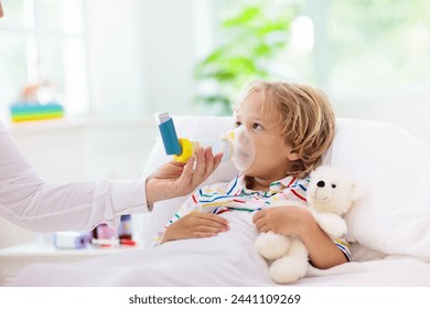 Sick little boy with medicine. Mother checking fever of ill child in bed. Unwell kid with chamber inhaler for asthma cough treatment. Flu season. Parent in bedroom or hospital room for young patient. - Powered by Shutterstock