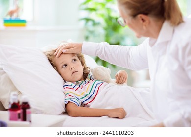 Sick little boy with medicine. Mother checking fever of ill child in bed. Unwell kid with chamber inhaler for asthma cough treatment. Flu season. Parent in bedroom or hospital room for young patient. - Powered by Shutterstock