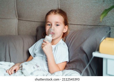 Sick Little Girl Making Inhalation With Nebulizer To Reduce Coughing, Lying In Bed At Home, Child Taking Medication While Breathing In Through Face Mask. Bronchitis And Asthma Treatments For Children