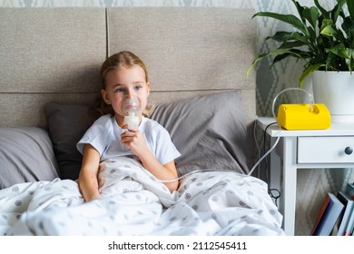 Sick Little Girl Making Inhalation With Nebulizer To Reduce Coughing, Lying In Bed At Home, Child Taking Medication While Breathing In Through Face Mask. Bronchitis And Asthma Treatments For Children