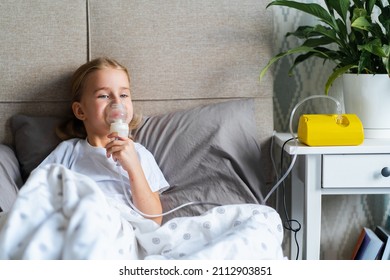 Sick Little Girl Making Inhalation With Nebulizer To Reduce Coughing, Lying In Bed At Home, Child Taking Medication While Breathing In Through Face Mask. Bronchitis And Asthma Treatments For Children