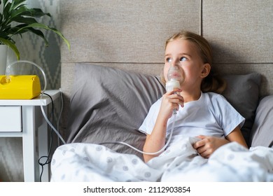 Sick Little Girl Making Inhalation With Nebulizer To Reduce Coughing, Lying In Bed At Home, Child Taking Medication While Breathing In Through Face Mask. Bronchitis And Asthma Treatments For Children