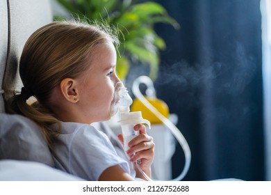 Sick little girl making inhalation with nebulizer to reduce coughing, lying in bed at home, child taking medication while breathing in through face mask. Bronchitis and asthma treatments for children