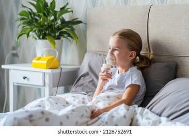 Sick Little Girl Making Inhalation With Nebulizer To Reduce Coughing, Lying In Bed At Home, Child Taking Medication While Breathing In Through Face Mask. Bronchitis And Asthma Treatments For Children