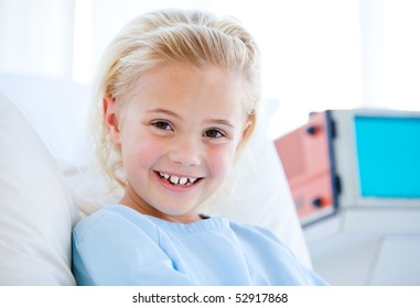 Sick Little Girl Smiling At The Camera Sitting On A Hospital Bed