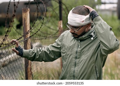 Sick Man With Bandage Around His Head Standing By Fence Net In Refugee Camp