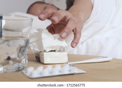 Sick Man In Bed With White Sheets. Above The Table Are Pills, Handkerchiefs, A Thermometer And A Glass Of Water.