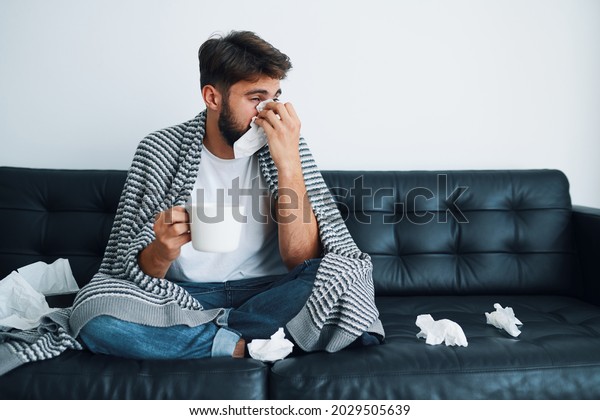 Sick man\
blowing running nose sitting on sofa at\
home