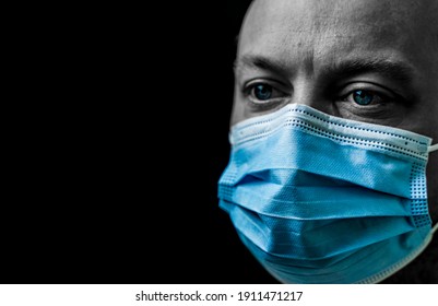 Sick Man With Bright Blue Eyes Wearing A Facemask, Portrait Isolated On Black With Shallow Depth Of Field.