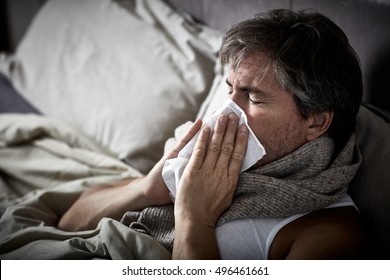 Sick Man With Cold Lying In Bed And Blow Nose.