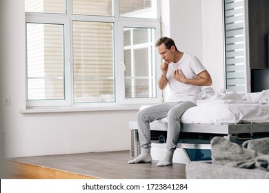 Sick Man Coughing While Sitting On Bed At Home