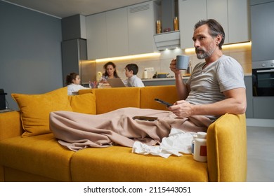 Sick Man Drinking Tea While Changing Channels With Remote