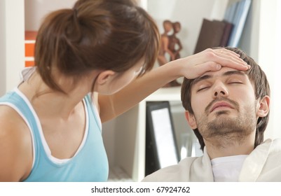 sick man with fever in bed - woman holding her hand on forehead