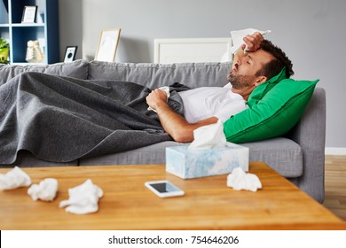 Sick Man With Fever Lying On Couch At Home