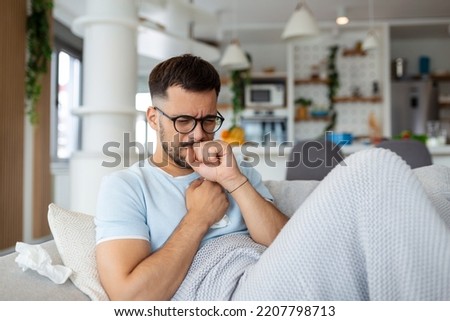 Sick man holding his chest in pain while coughing in the living room. Sore throat and cough, man with lung pain at home, health problems concept