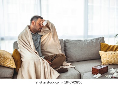 Sick Man Lying On Sofa At Home In Living Room. Middle Age Man Feeling Sick With Cold And Fever At Home, Ill With Flu Disease Sitting On The Sofa. It's The Season Of Sneezes