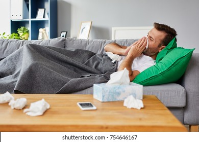Sick man lying on sofa at home and blowing nose - Shutterstock ID 754646167