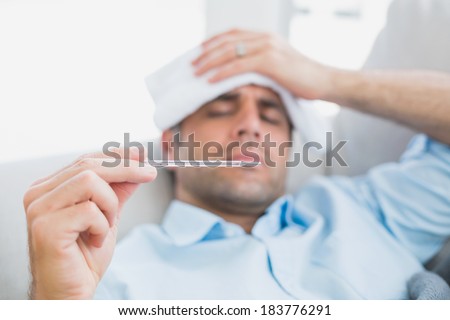 Sick man lying on sofa checking his temperature at home in the living room