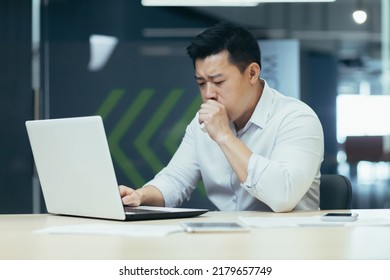 Sick Man In Office Coughs And Has Runny Nose, Asian Businessman With Cold Works In Office On Laptop