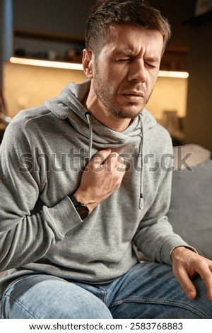 Sick man sitting on sofa at home, coughing, suffering from chest pain and respiratory issues, Symptoms of flu, asthma, or bronchitis. Illness, infection, and sickness concept