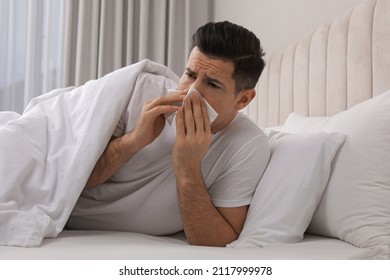 Sick Man With Tissue Suffering From Cold In Bed At Home