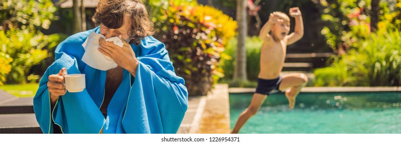 Sick Man Traveler. The Man Caught A Cold On Vacation, Sits Sad At The Pool Drinking Tea And Blows His Nose Into A Napkin. His Son Is Healthy And Swimming In The Pool. Travel Insurance Concept BANNER