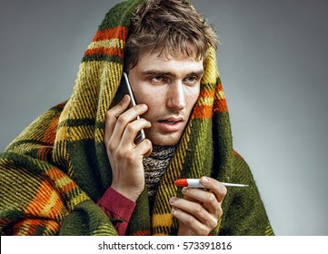 Sick Man Wrapped In Blanket With A High Temperature Calling On The Phone. Man Suffering Cold And Winter Flu Virus. Health Care Concept