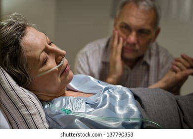 Kranke reife Frau, die im Bett liegt, besorgter Ehemann mit Händen