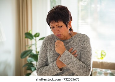 Sick mature woman with sore throat, standing in living room at home. Catching cold, having cough. - Powered by Shutterstock