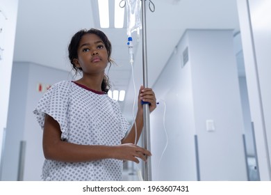 Sick Mixed Race Girl Walking In Hospital Corridor With Iv Drip Bag On Stand. Medicine, Health And Healthcare Services.