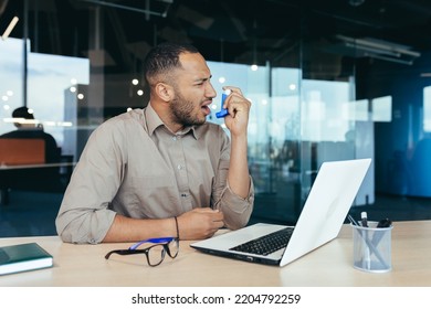 Sick Office Worker With Asthma Having Trouble Breathing, Man Using Inhaler To Relieve Breathing, Hispanic Man Working Inside Modern Office Building, Mixed Race Man With Laptop.