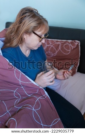 Sick old woman lying in bed at home feel sick suffer from flu or cold cure with prescribed medications. Woman drinking from a glass