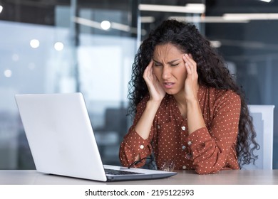 Sick And Overtired Latin American Business Woman Working Inside Office Building, Female Worker Holding Her Head With Hands Having Severe Headache And Migraine