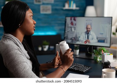 Sick Patient Holding Bottle Of Pills On Video Call With Medic, Doing Remote Online Consultation On Computer. Woman Asking Doctor About Healthcare Treatment On Video Conference At Home.