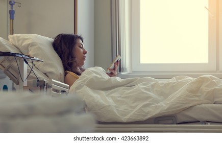 A Sick Patient Lying In A Hospital Bed With A Mobile Phone.