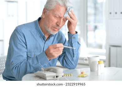 A sick person feels the symptoms of a viral disease, holds a thermometer in his hand. Tablets and water on the table. High quality photo
