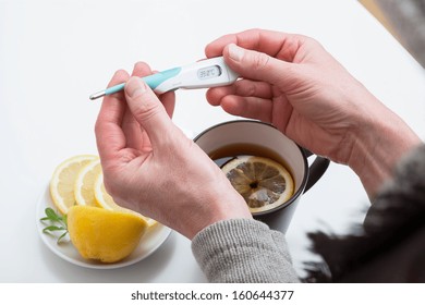 Sick Person Who Is Looking At Thermometer And Drinking Hot Tea With Lemon