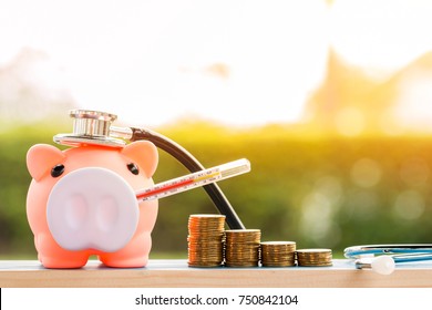 Sick piggy bank use thermometer fever and stethoscope check hygiene and stack coin put on the wood on sunlight in the public park, saving money for buy health insurance concept. - Shutterstock ID 750842104