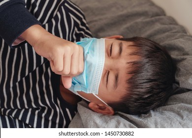 Sick Preteen Asian Boy Wearing Medical Face Mask And Coughing In Bed, Self Quarantine, Long Covid, Influenza, Pneumonia, Tuberculosis, Asthma, Chest And Heal