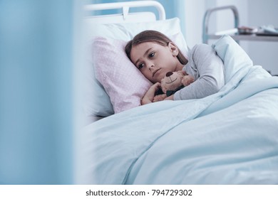 Sick, Sad Girl With A Teddy Bear Lying In A Hospital Bed Alone And Scared