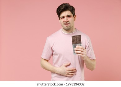 Sick Sad Unhealthy Ill Allergic Man Has Red Watery Eyes, Runny Stuffy Sore Nose Suffer From Allergy Trigger Symptoms Feel Bad Hold In Hand Chocolate Bar Isolated On Pastel Pink Color Background Studio