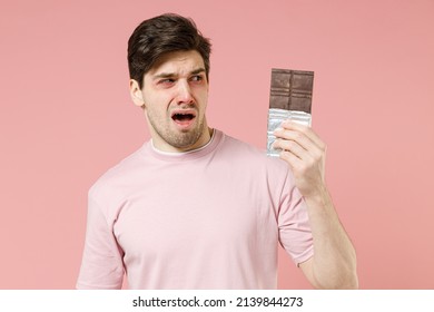 Sick Sad Unhealthy Ill Allergic Man Has Red Watery Eyes, Runny Stuffy Sore Nose Suffer From Allergy Trigger Symptoms Feel Bad Hold In Hand Chocolate Bar Isolated On Pastel Pink Color Background Studio