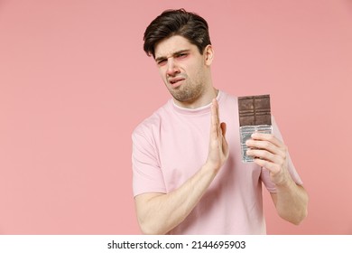 Sick Sad Unhealthy Ill Allergic Man Has Red Watery Eyes, Runny Stuffy Sore Nose Suffer From Allergy Trigger Symptoms Feel Bad Hold In Hand Chocolate Bar Isolated On Pastel Pink Color Background Studio