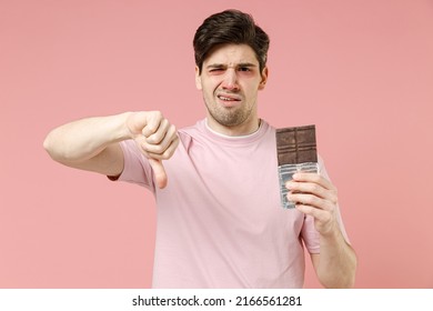 Sick Sad Unhealthy Ill Allergic Man Has Red Watery Eyes, Runny Stuffy Sore Nose Suffer From Allergy Trigger Symptoms Feel Bad Hold In Hand Chocolate Bar Isolated On Pastel Pink Color Background Studio