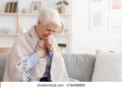 Sick Senior Woman Covered In Blanket Coughing Hard At Home, Having Coronavirus Symptomes, Sitting On Couch In Living Room, Copy Space - Powered by Shutterstock